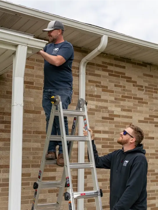 Two maintenance workers working, one holding a ladder while the other stands on the ladder.